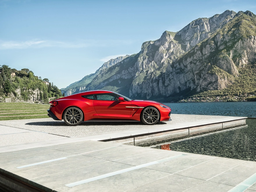 Красный автомобиль Aston Martin на фоне озера и гор