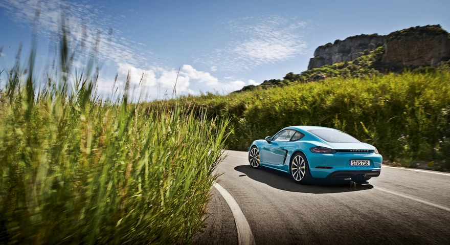 Голубой Porsche Cayman едет по дороге