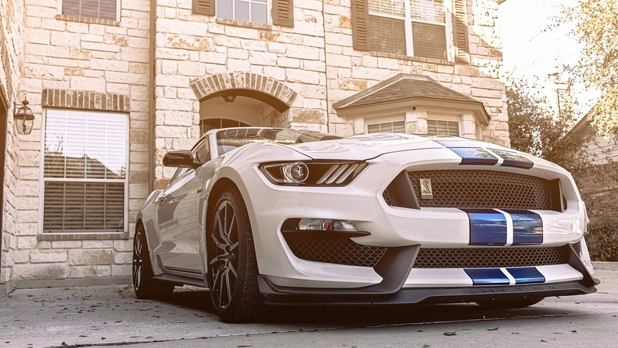 Белый Ford Mustang на фоне здания