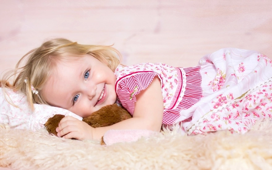 Девочка лежит на мягком пледе обнявшись с игрушкой