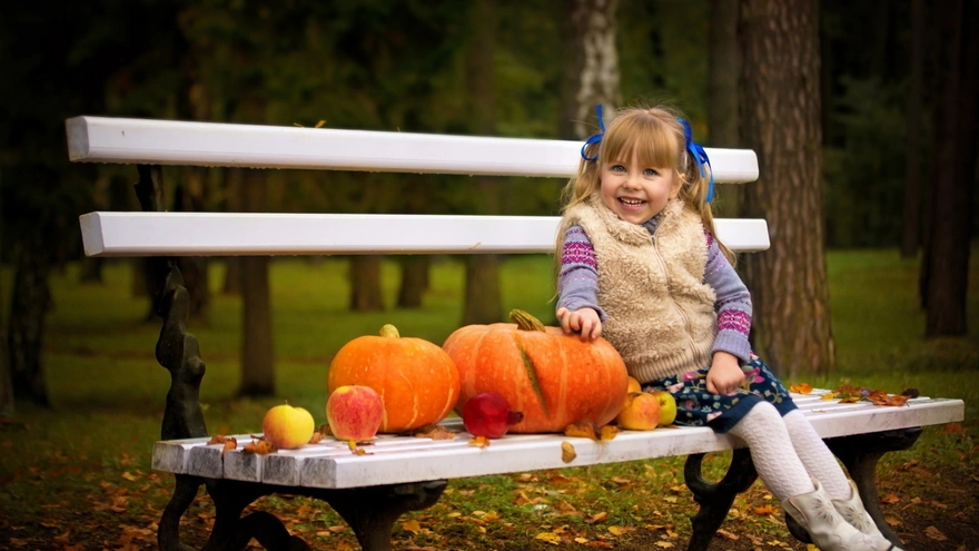 Улыбающаяся девочка сидит на скамейке с дарами осени