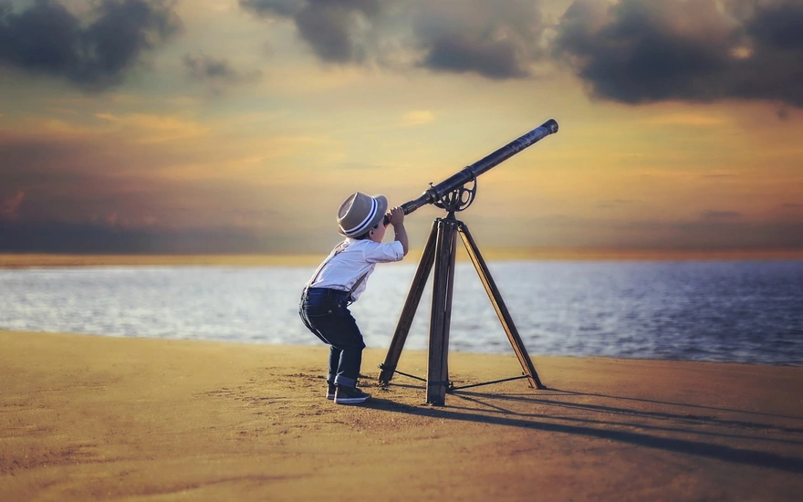 Маленький мальчик смотрит в телескоп на небо