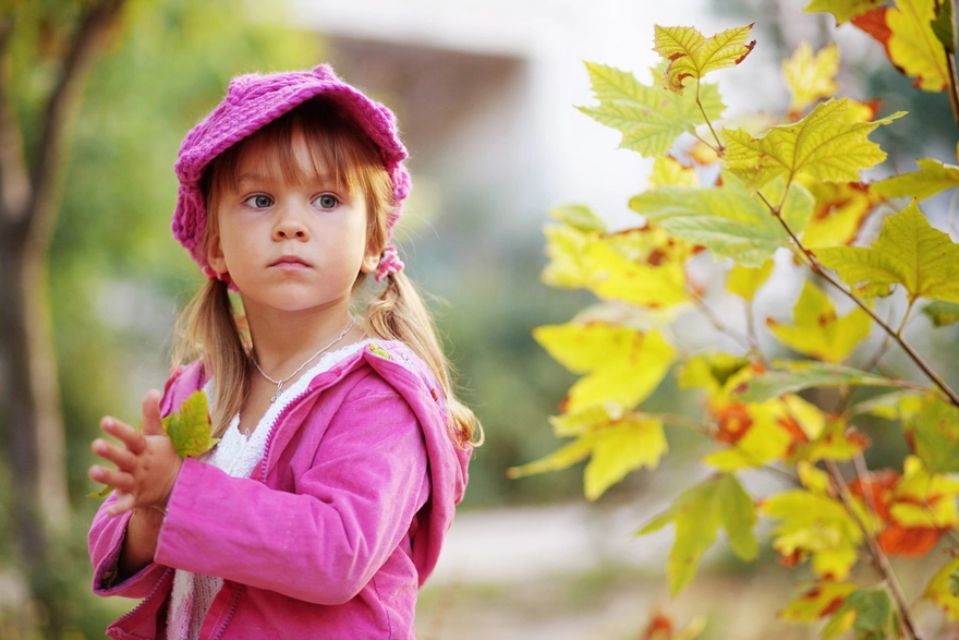 Девочка в розовом одеянии держит листик в руках, смотря куда-то.
