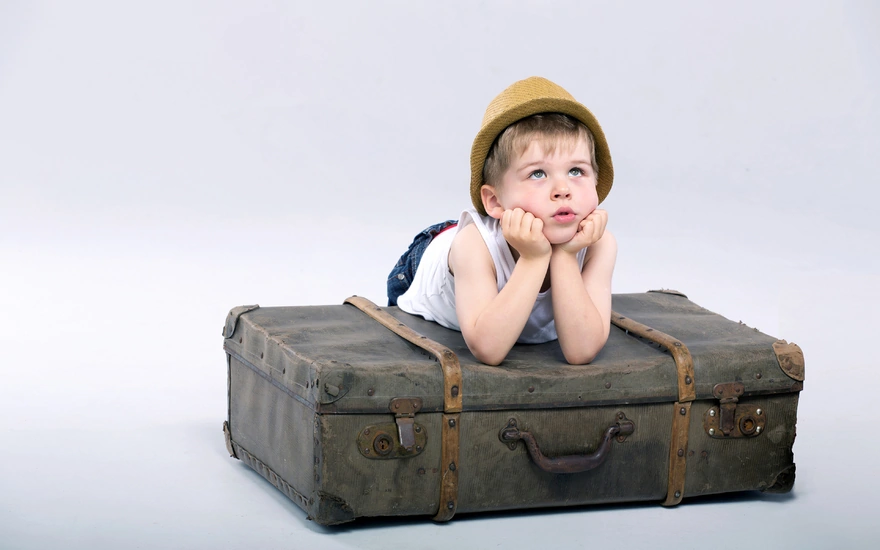 Мальчик упёрся локтями в чемодан и смотрит на верх