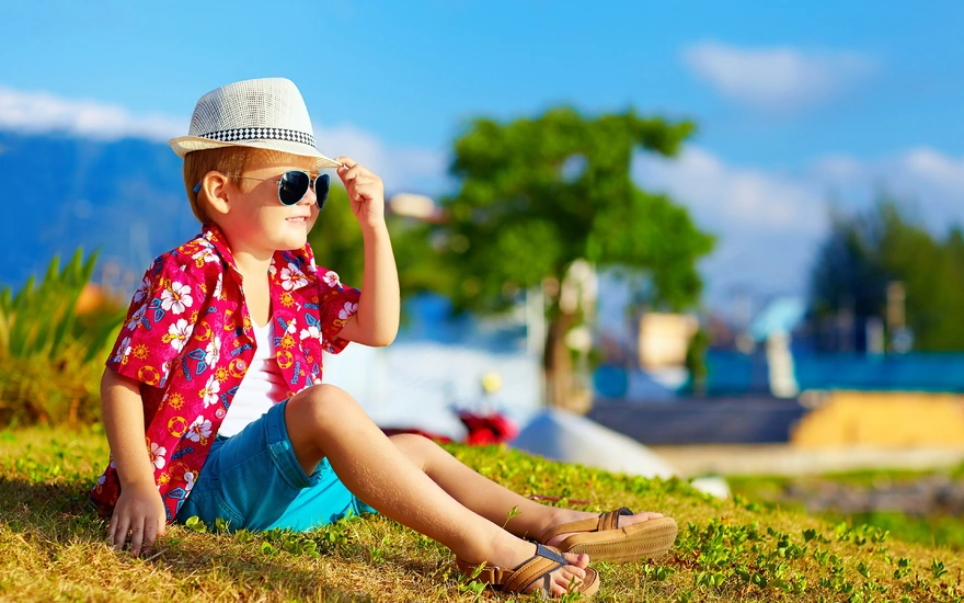 Boy in hat and glasses sitting on the grass looking into the distance
