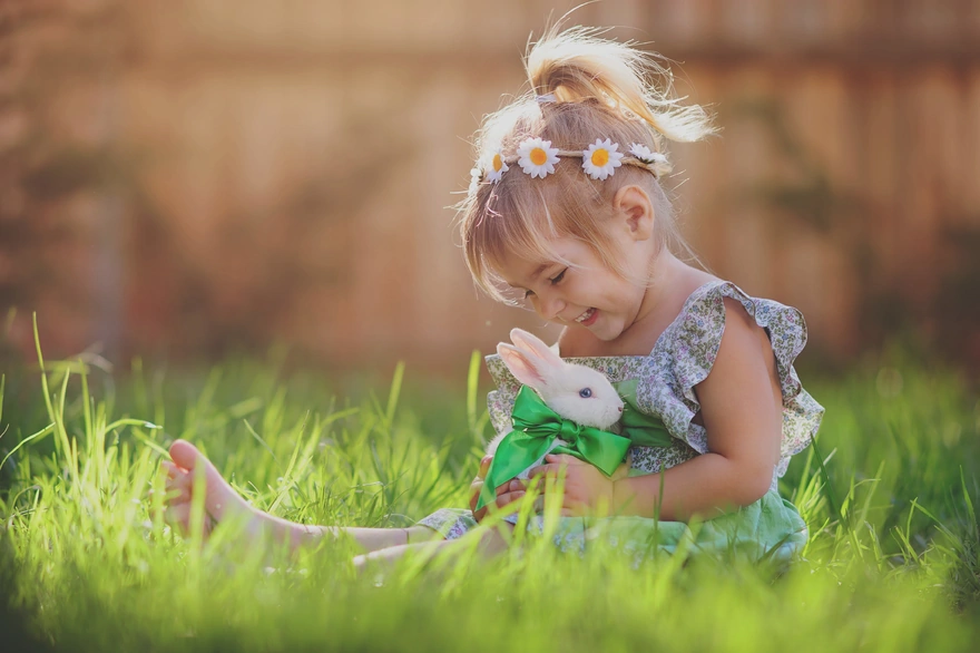 Маленькая девочка сидит в траве с кроликом