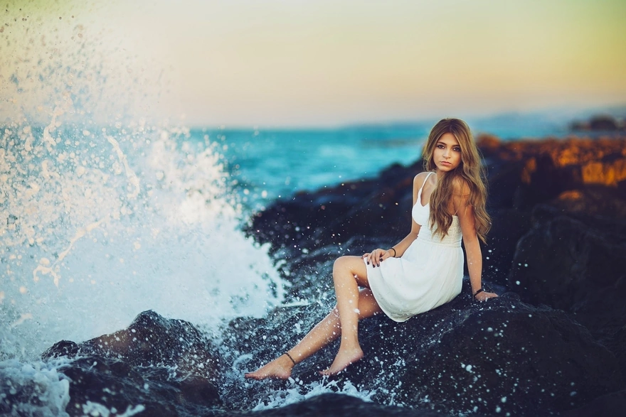 Девушка сидит на камнях у моря