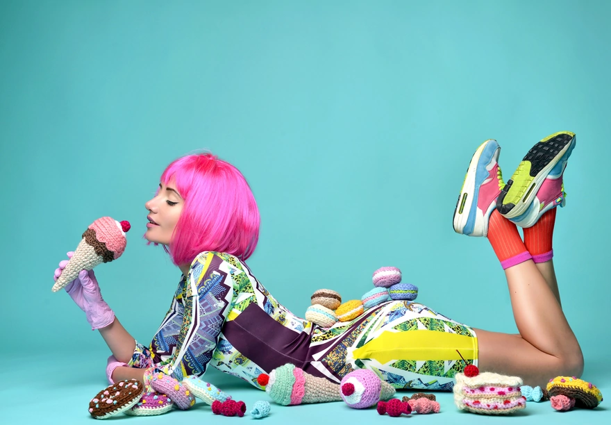 Девушка с розовыми волосами лежит возле вязаных вкусностей