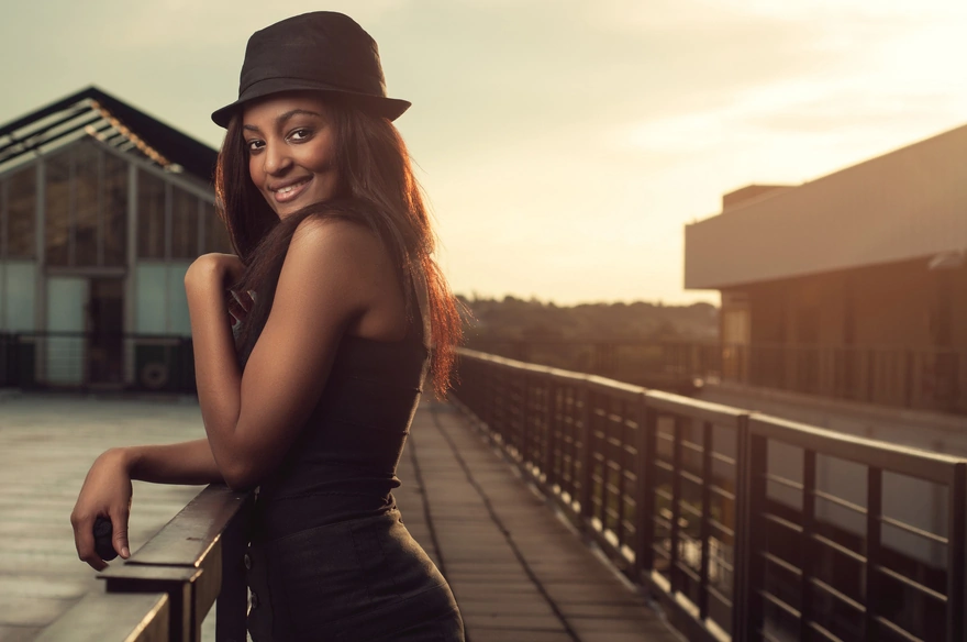 Чернокожая девушка с красивой улыбкой в шляпке стоит на мостике