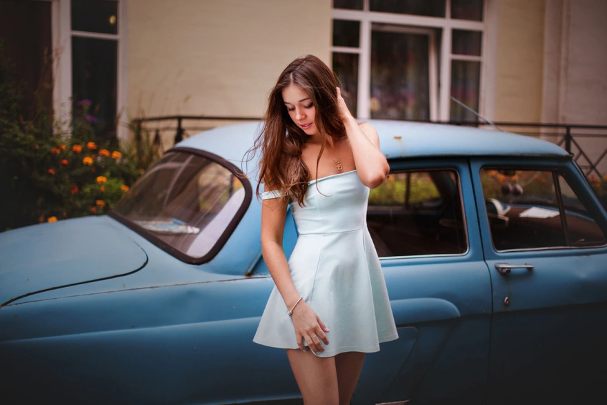 A girl in a dress poses against the backdrop of a retro car
