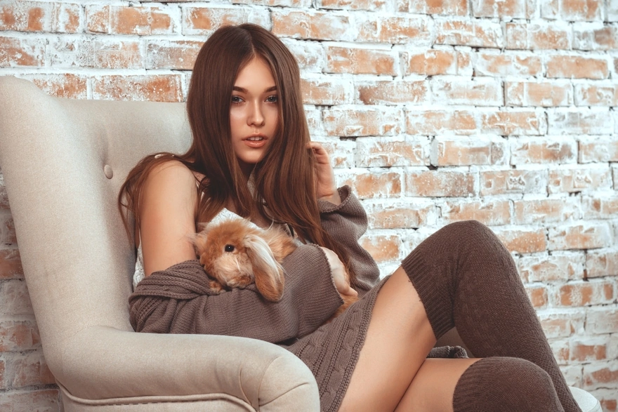 Brunette in a chair with a rabbit against a brick wall