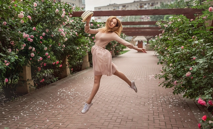 Девушка в прыжке на фоне красивых кустовых роз