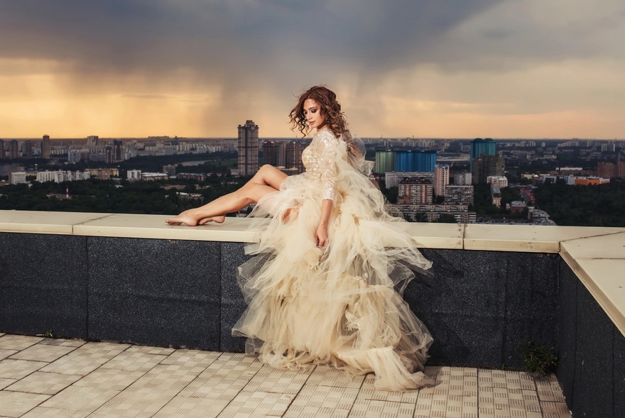 Девушка в красивом платье сидит на крыше с видом на город