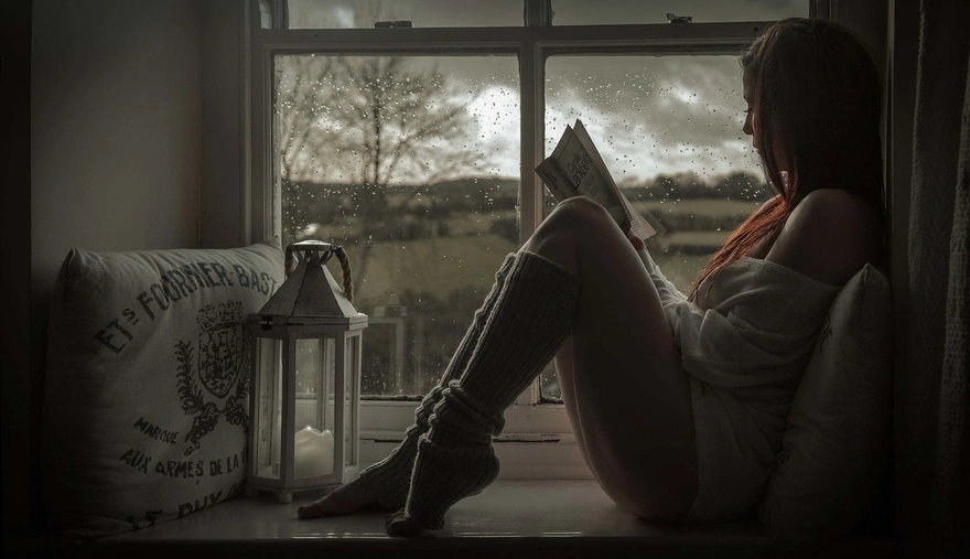 The girl sitting on the windowsill reading a book