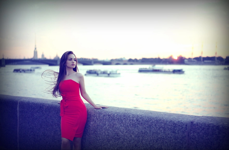 Девушка в красном платье позирует на набережной