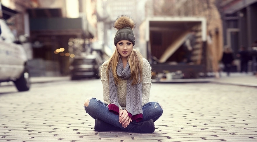 Девушка сидит на тротуаре в шапке