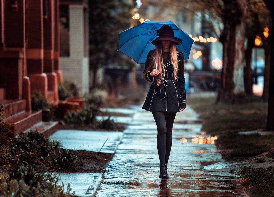 Девушка в шляпе и плаще идёт под зонтом в дождливую погоду