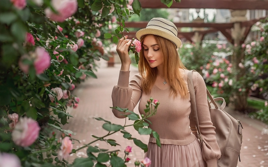 Девушка в розовом платье и шляпке позирует у роз
