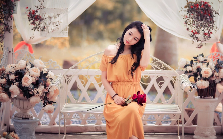 Азиатка сидит на скамейке с розой
