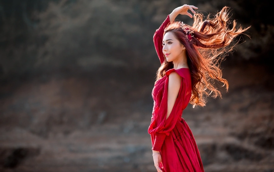 У азиатки в красном платье волосы развиваются на ветру