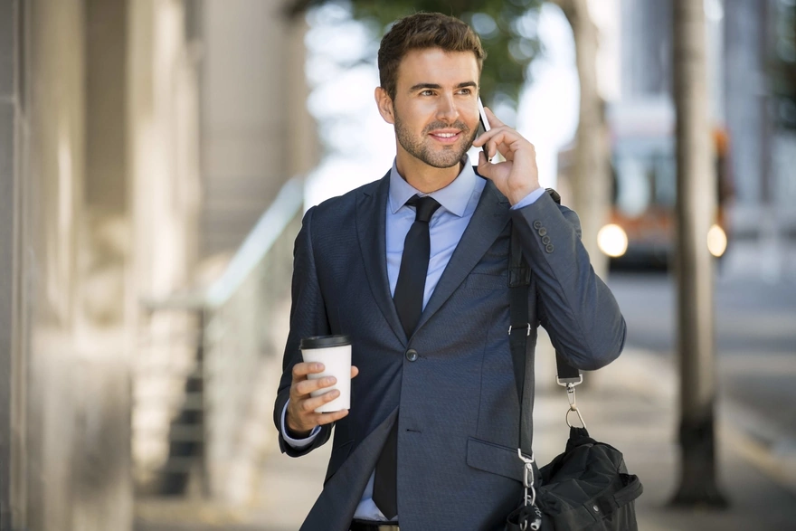 Стильный мужчина в костюме держит стаканчик кофе в руке и разговаривает по телефону