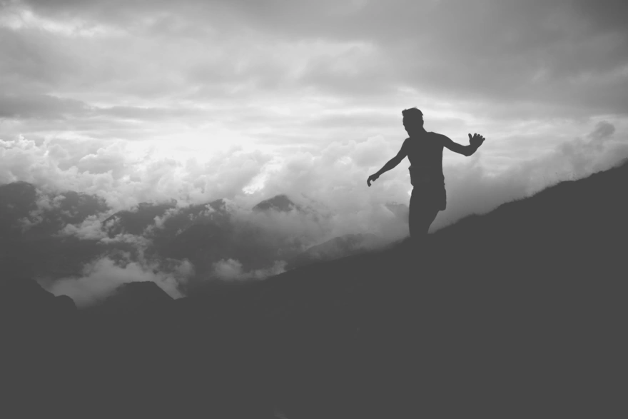 Мужчина идёт по склону горы держа равновесие руками