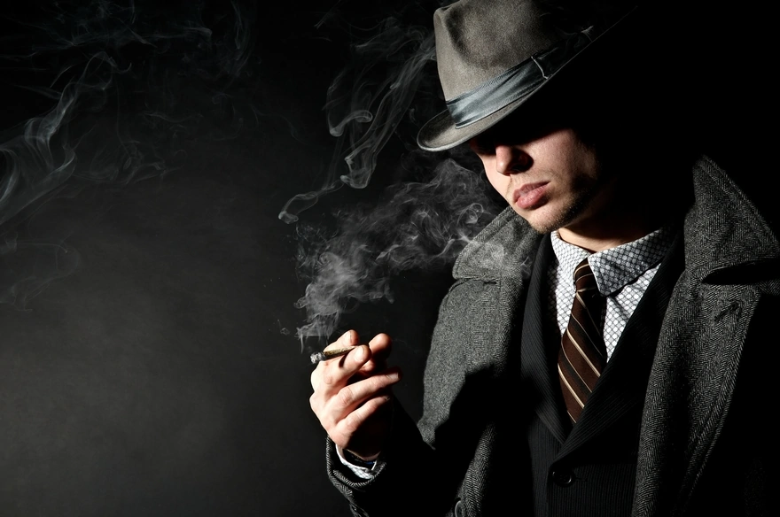 Мужчина в пальто и шляпе курит сигару