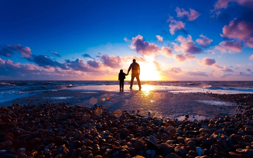 Папа с сыном прогуливаются по берегу моря на закате солнца