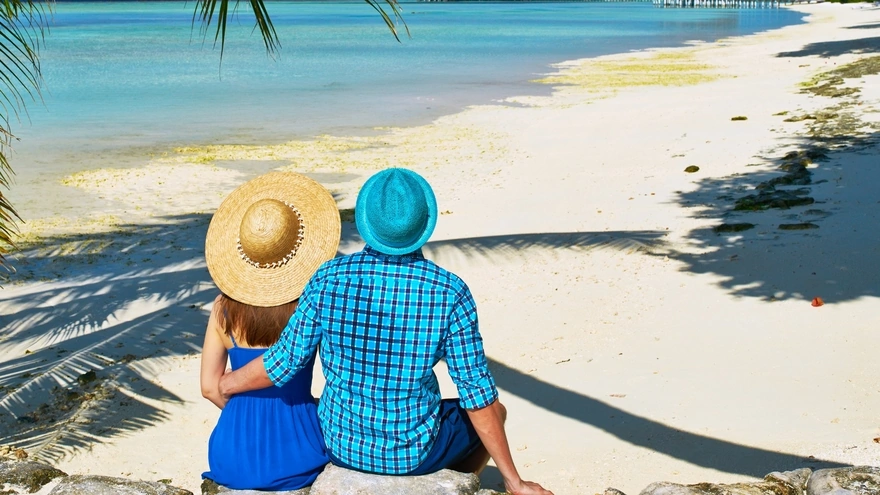 Молодая пара сидит на пляже в тропиках любуясь на море