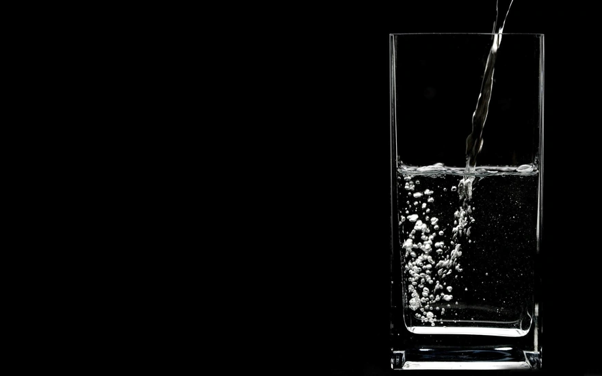 В стакан на чёрном фоне наливают чистую прозрачную воду