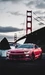 Картинка: Красный автомобиль с включёнными фарами на фоне навесного моста
