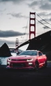 Картинка: Красный автомобиль с включёнными фарами на фоне навесного моста