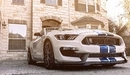 Картинка: Белый Ford Mustang на фоне здания.