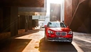 Картинка: Ярко-красный BMW в солнечных лучах, окруженный зданиями.