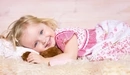 Картинка: Девочка лежит на мягком пледе обнявшись с игрушкой.