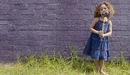 Картинка: Девочка с вертушкой в руках стоит возле стены