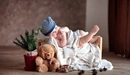 Картинка: Малыш в шапочке лежит среди игрушек