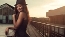 Картинка: Чернокожая девушка с красивой улыбкой в шляпке стоит на мостике.