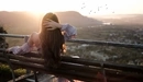 Картинка: Девушка, сидя на скамейке и держа руку за головой, любуется закатом солнца.