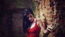 Картинка: Девушка с чёрными волосами в красном стоит упираясь в кирпичную стену