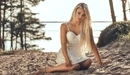 Картинка: Блондинка сидит на песке в хвойном лесу рядом с озером