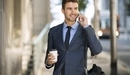 Картинка: Стильный мужчина в костюме держит стаканчик кофе в руке и разговаривает по телефону.