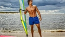 Картинка: Мужчина стоит на берегу со своей парусной доской (виндсёрф) для виндсёрфинга.