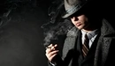 Image: Man in coat and hat smoking a cigar.