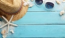 Картинка: Плетёная шляпа с очками лежат среди ракушек.