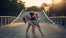 Image: Two gymnasts hold the ball with their backs while standing on the bridge.