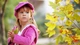 Картинка: Девочка в розовом одеянии держит листик в руках, смотря куда-то.
