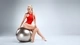 Картинка: Блондинка с красивой фигурой сидит на фитнес мяче в красном купальнике