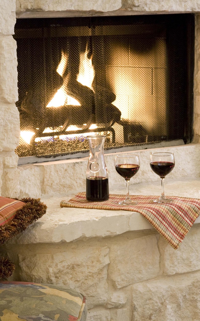 Image: Fireplace, fire, stone, striped pillows, decanter, wine glasses, books